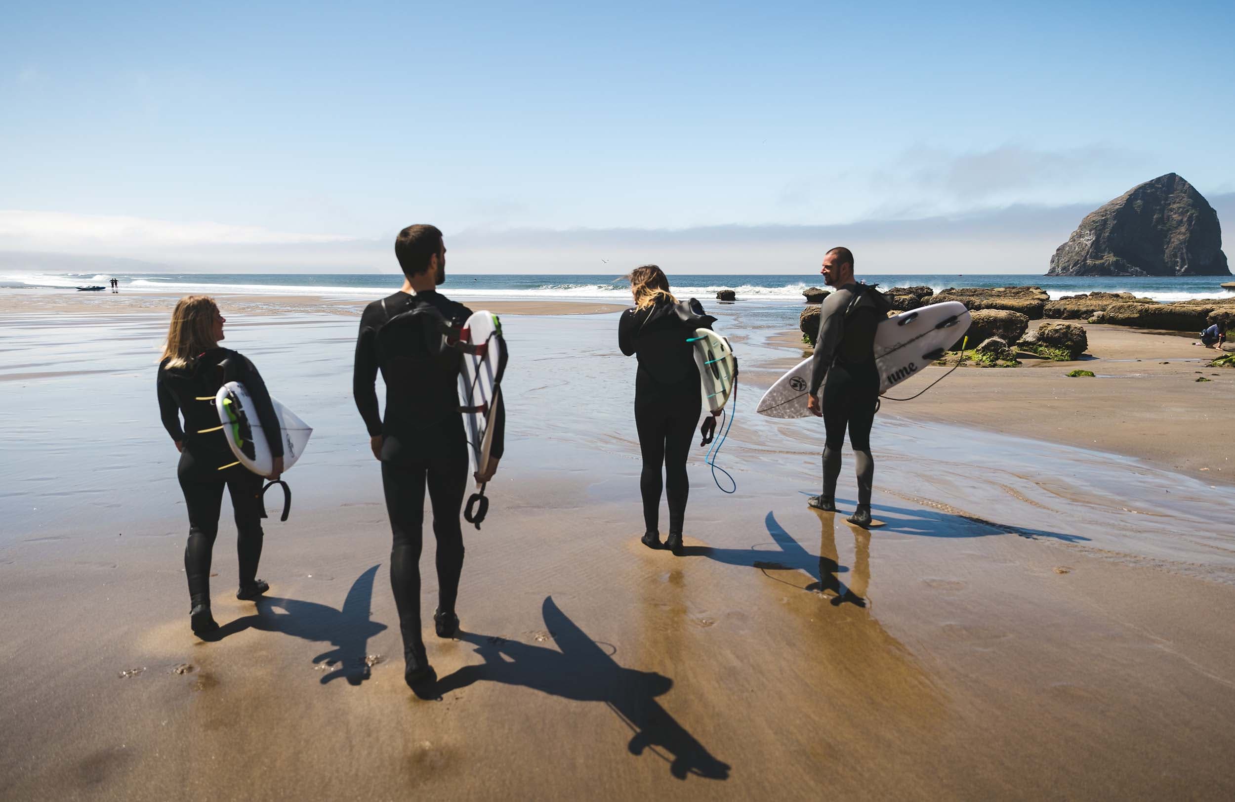 4 people walking on the beach at Cape Kiwanda with surfboards going to surf