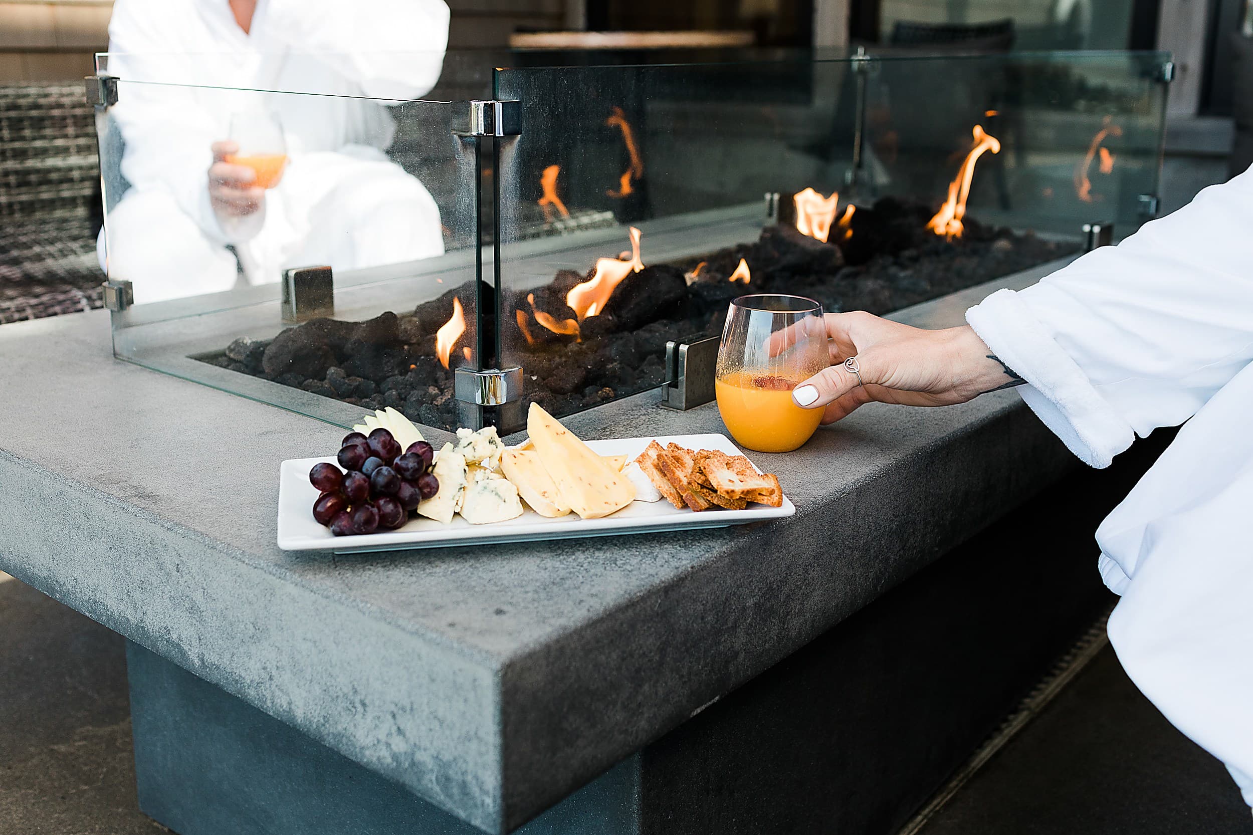 Guests in plush robes enjoying a charcuterie board and mimosas by the outdoor fire pit at Headlands Coastal Lodge & Spa, Oregon Coast
