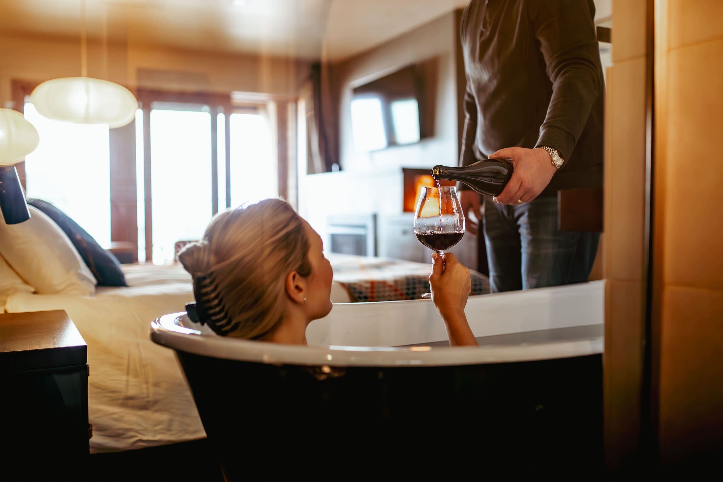 A man pouring a glass of wine for a woman in a tub at Headlands