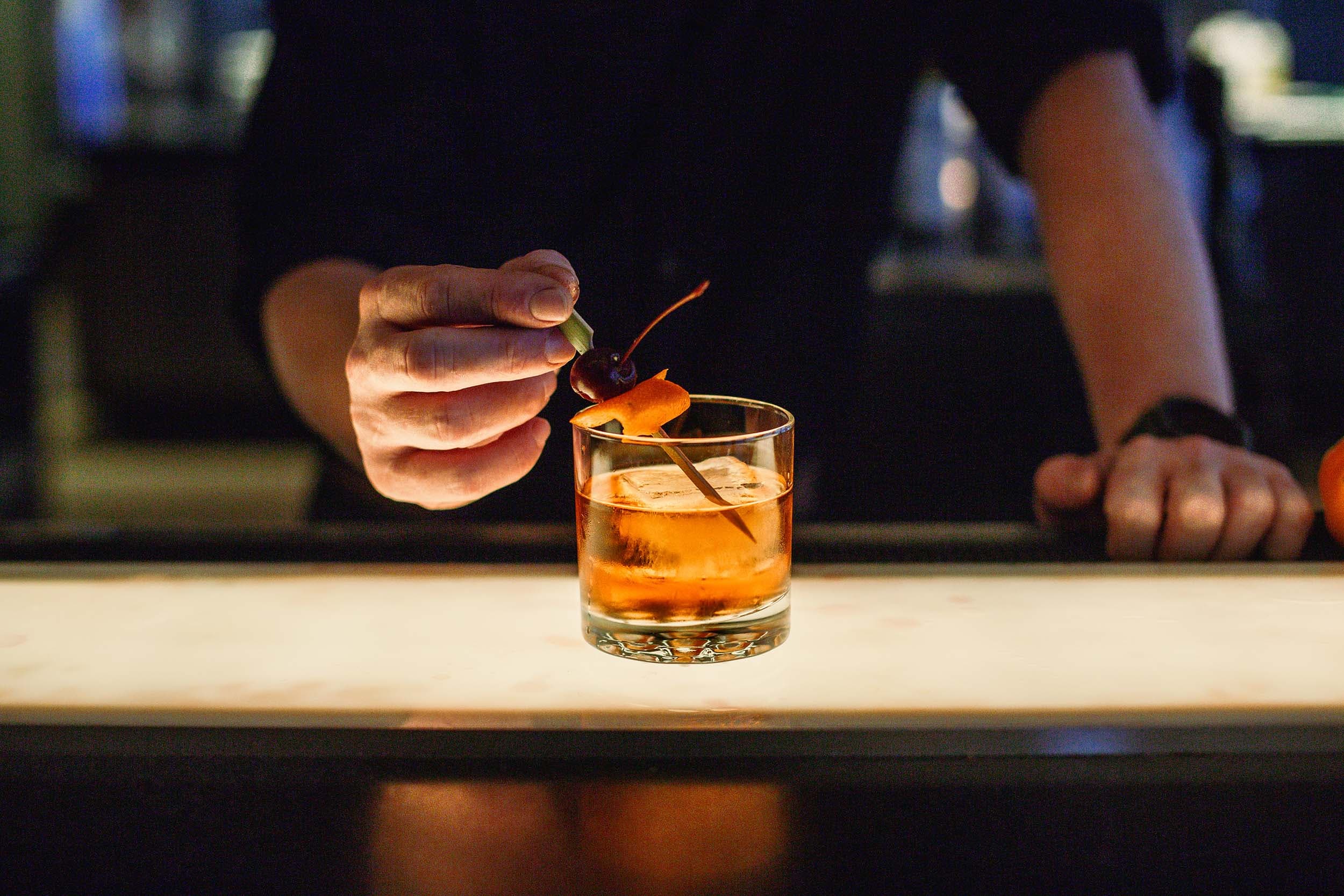 A negroni on a bar top with an orange rind and a cherry