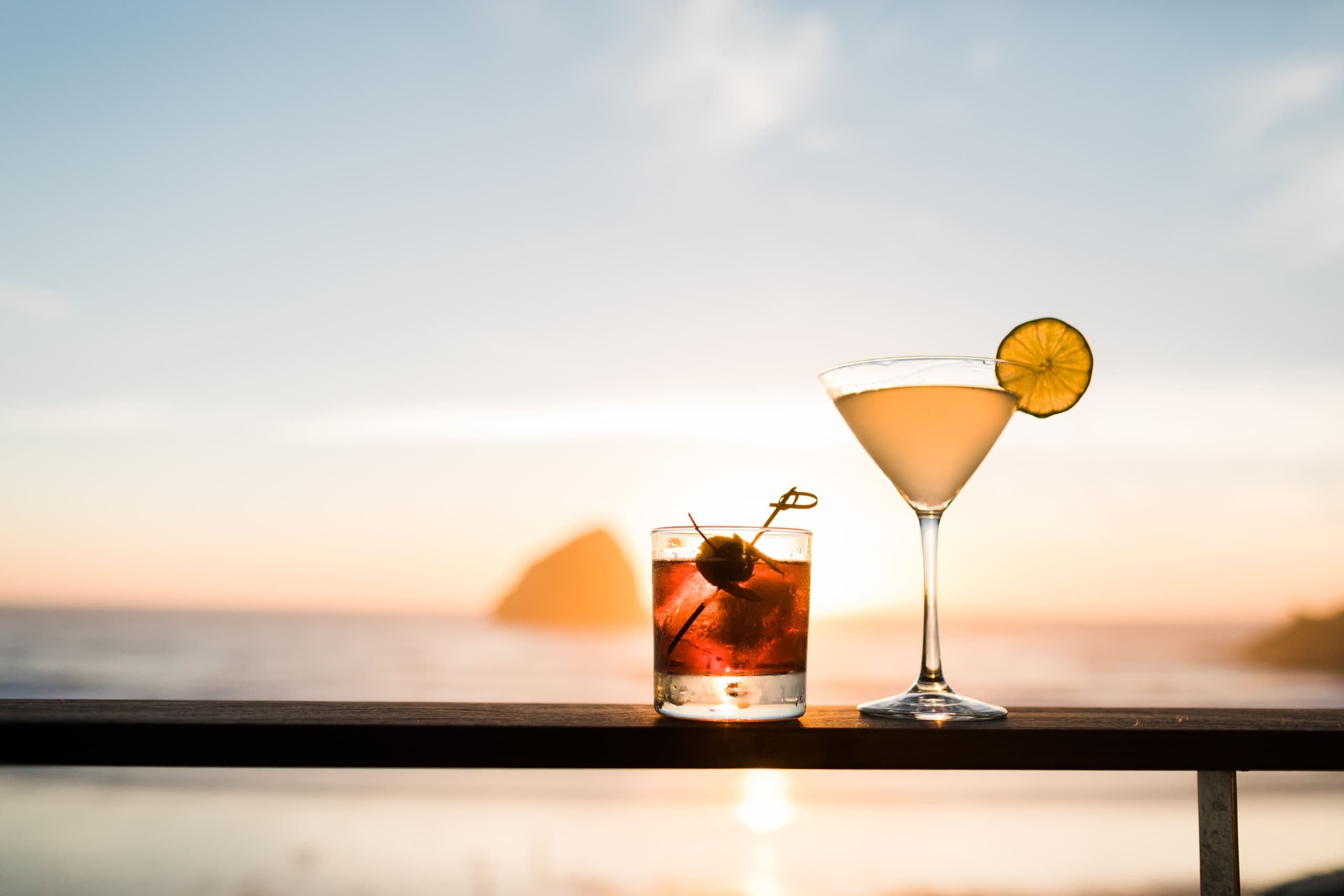 Two cocktails on the railing of a balcony with Haystack Rock in the background