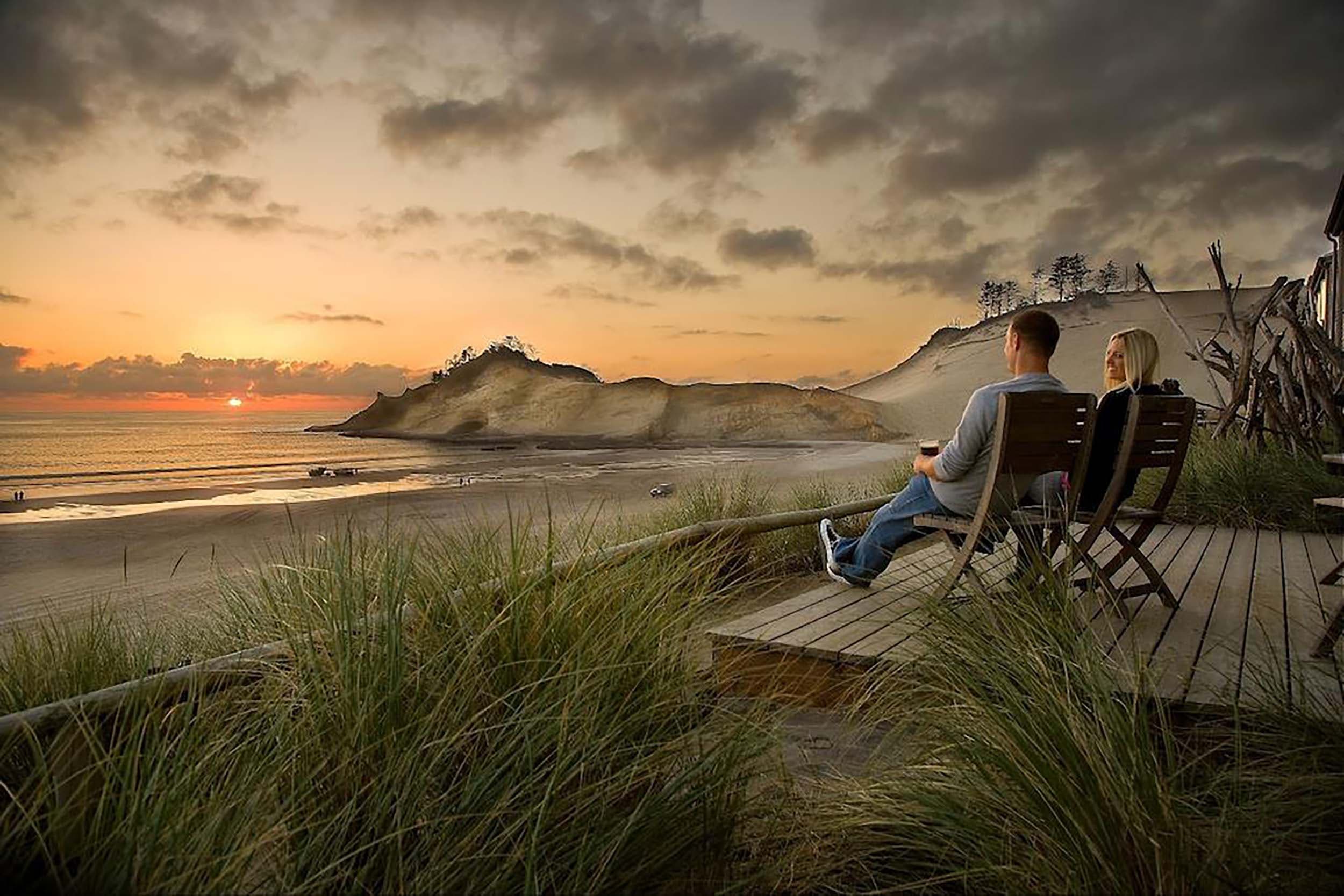 A couple sitting on the room patio looking out to the beach at sunset at Headlands