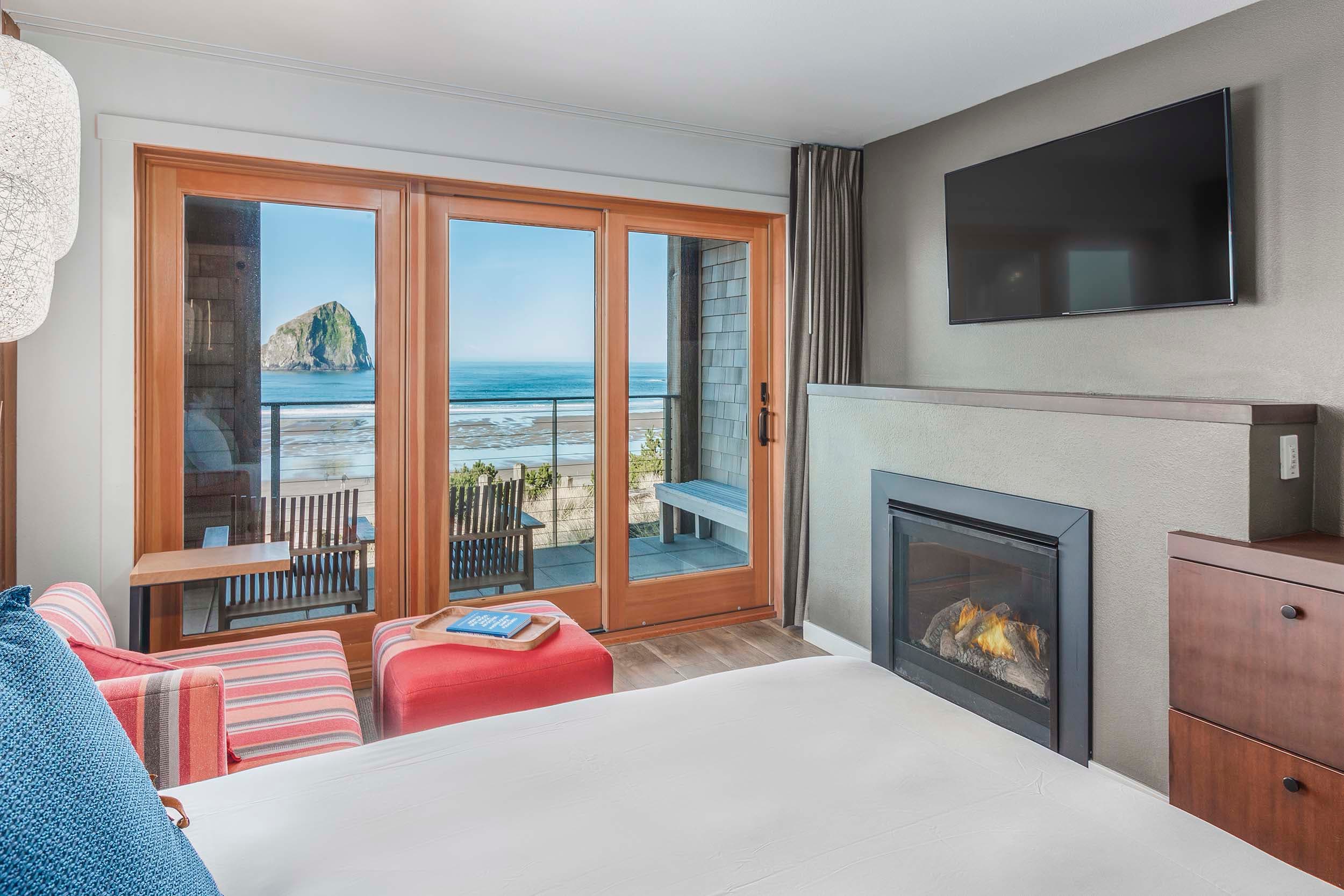 A queen bed, fireplace, living space, and a balcony with a view of the ocean in a Two Queens Sunlight lodge at Headlands