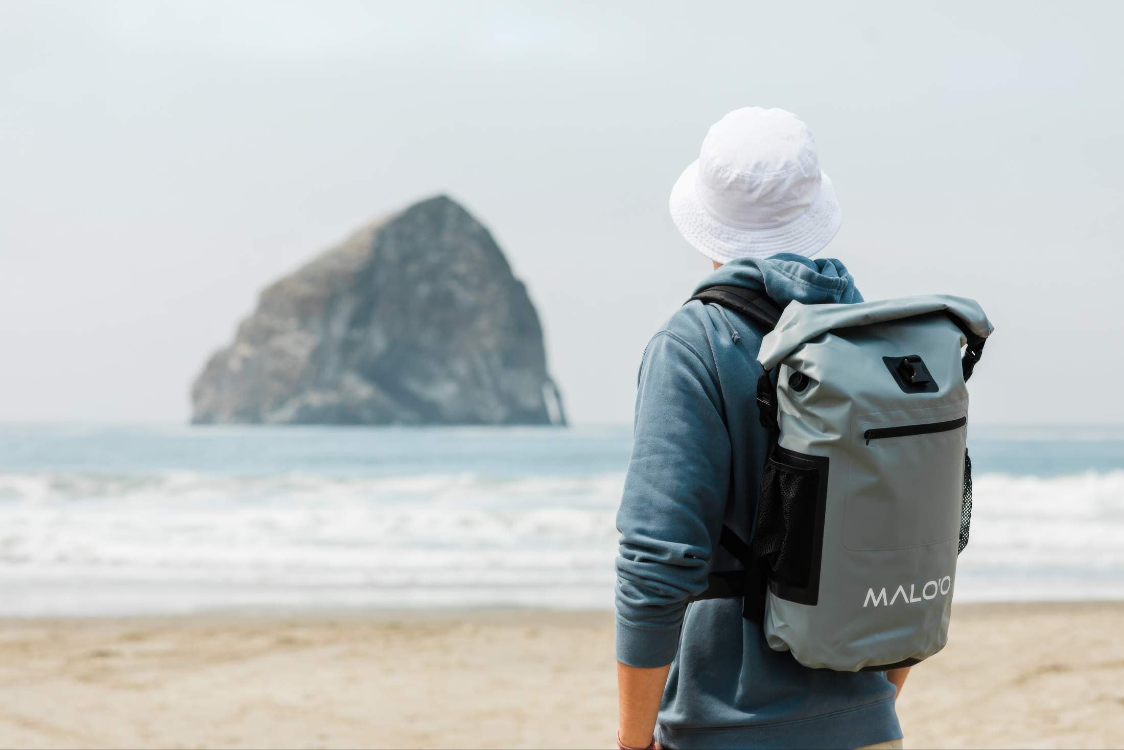 A man in a bucket hat and a backpack walking on the beach near Headlands