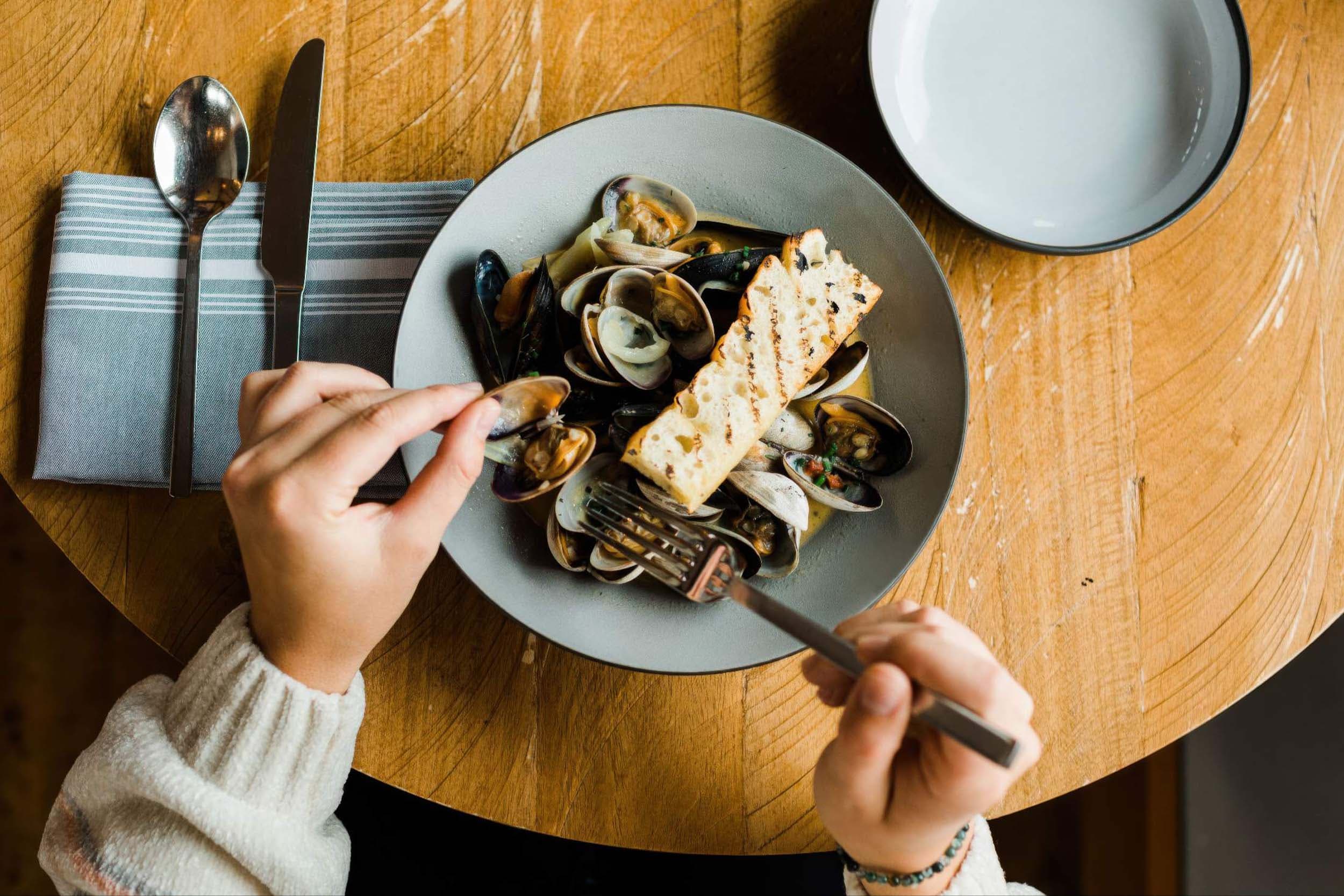 A person eating a bowl of clams at Meridian restaurant near Headlands
