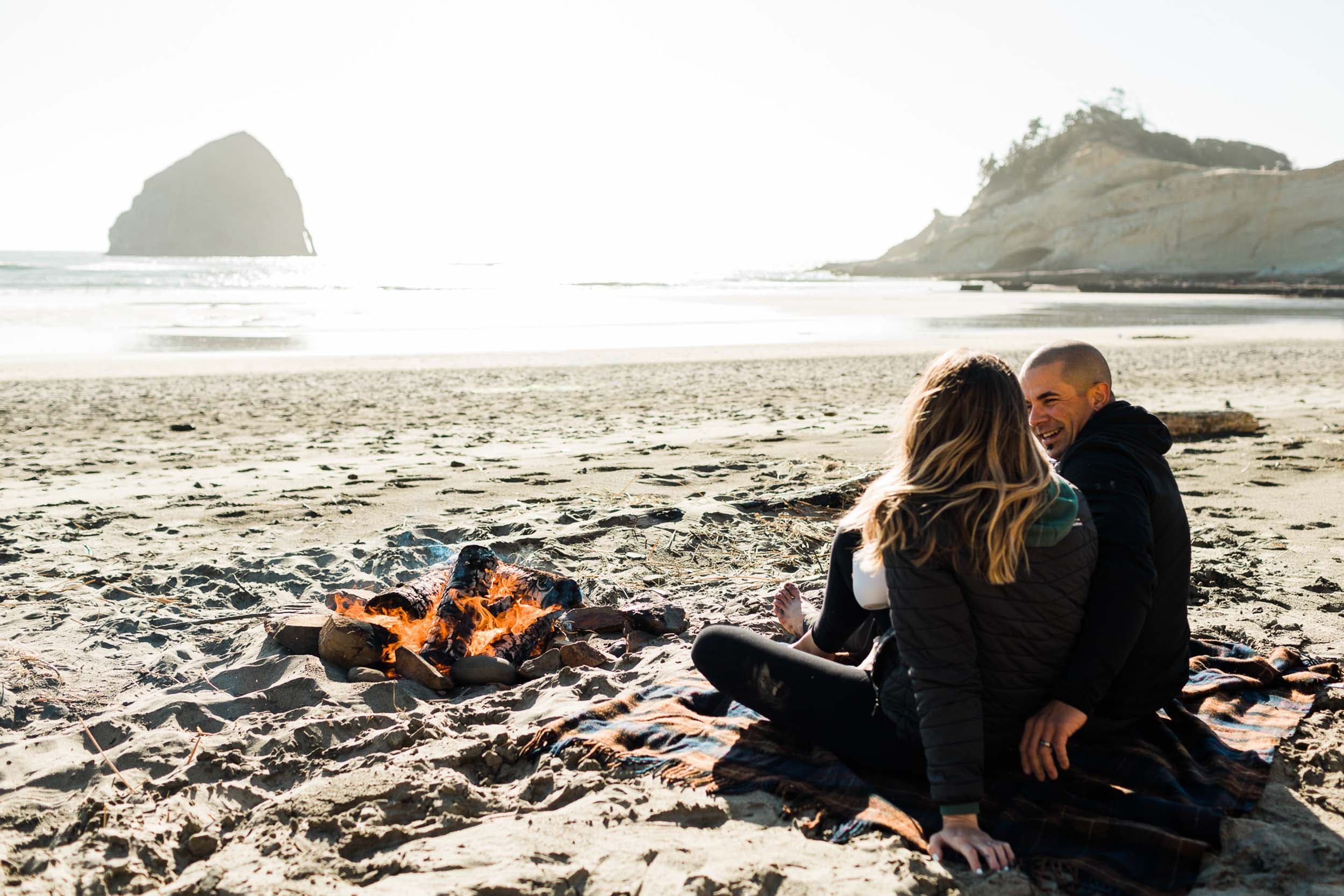 A couple sitting on the beach in front of a fire at Cape Kiwanda