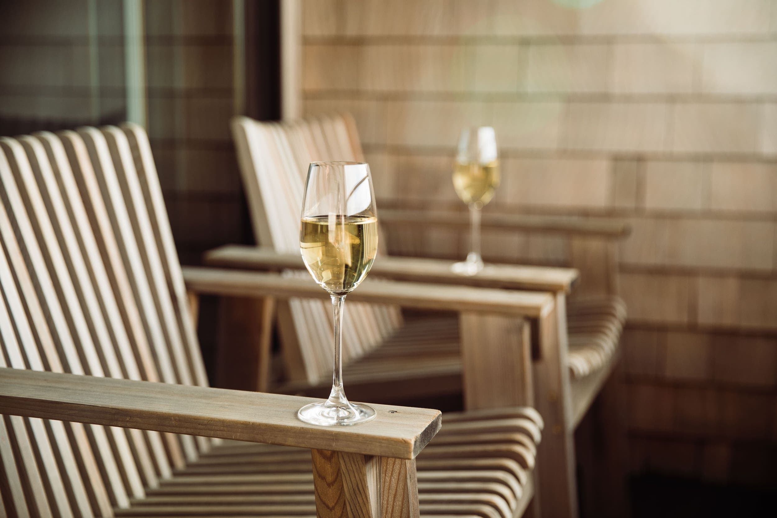 Two wooden chairs on a private patio with 2 glasses of white wine