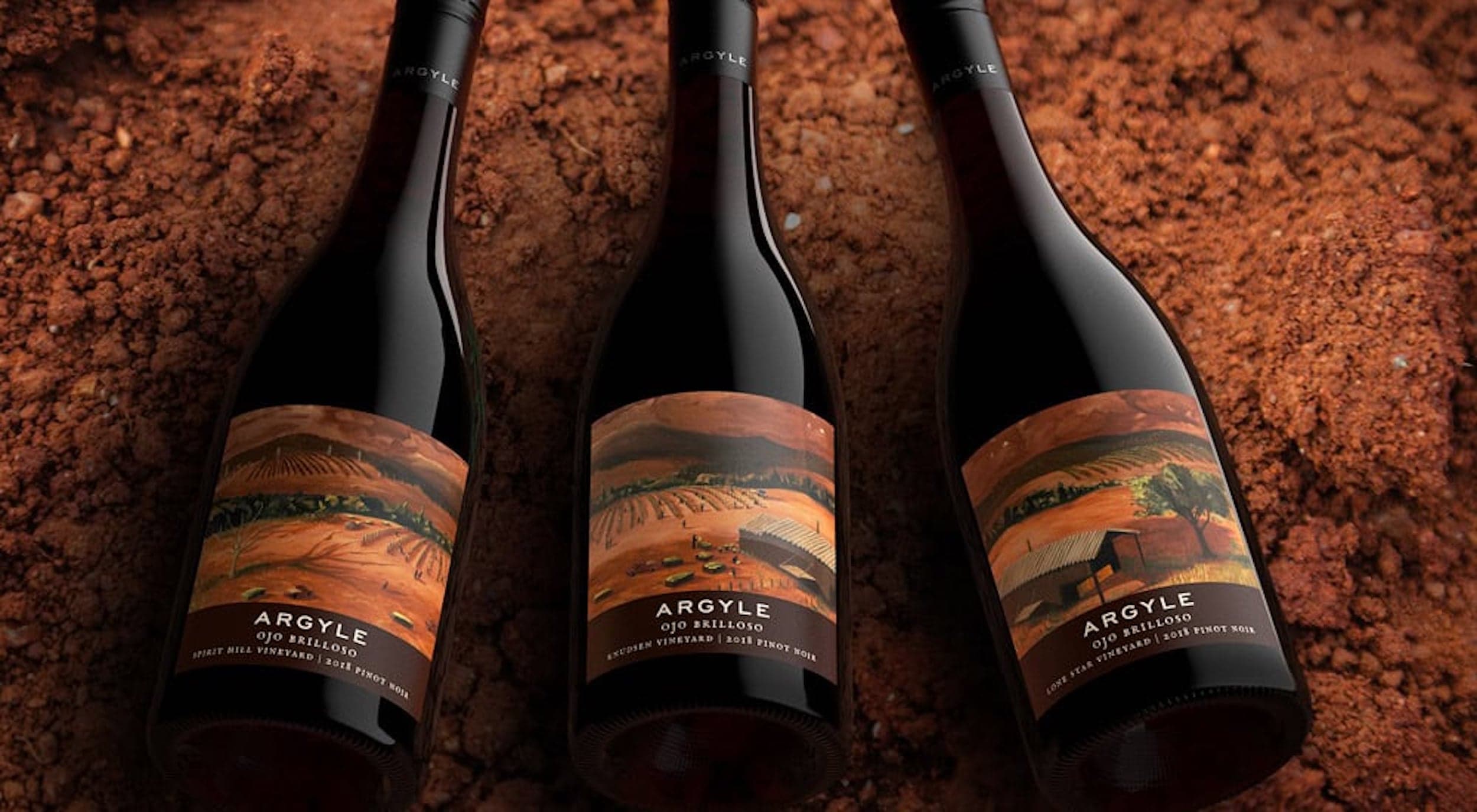 Three bottles of Argyle red wine laying on some red dirt