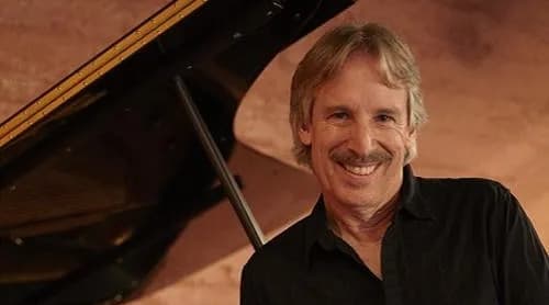 John Nilsen leaning on a piano smiling